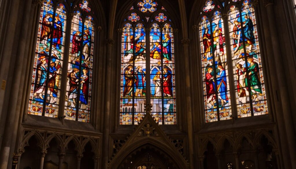 A close-up view of the stunning stained glass windows of Sainte-Chapelle, capturing the intricate designs and vivid colors that depict biblical scenes. In the foreground, shimmering light filters through the glass, casting colorful reflections onto the stone floor. The middle ground showcases a majestic view of the ornate gothic architecture, highlighting delicate stone carvings and the iconic pointed arches. In the background, faint silhouettes of medieval Paris can be seen through the windows, enhancing the atmosphere of the historical setting. The scene is bathed in warm, golden lighting, reminiscent of late afternoon sun, creating a serene and spiritually uplifting mood. Shot with a 35mm fast prime lens to emphasize detail and depth, presenting a hyperrealistic representation with a touch of harsh analog chaos.